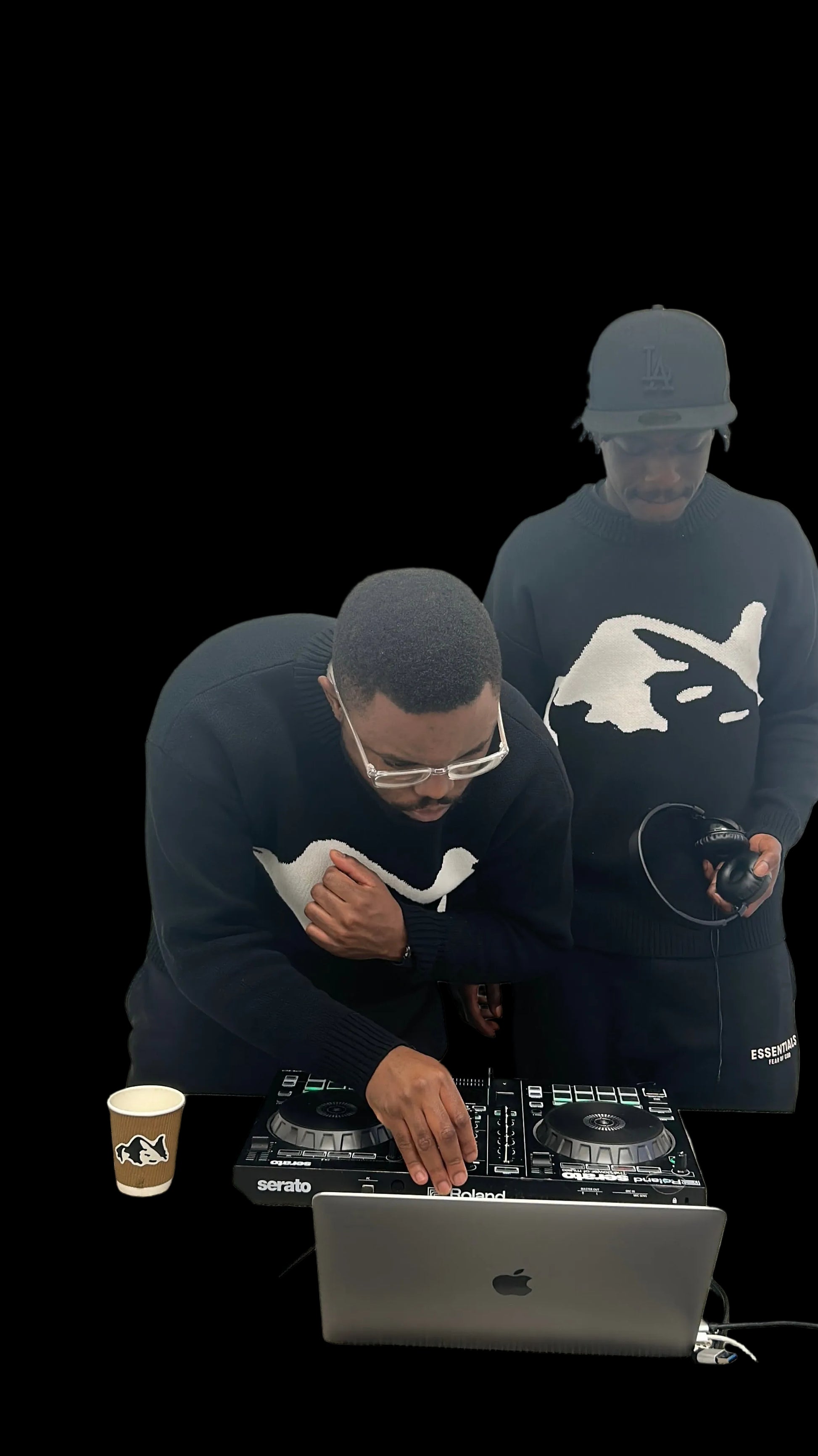 Two people using DJ equipment with a laptop on a table against a plain wall.